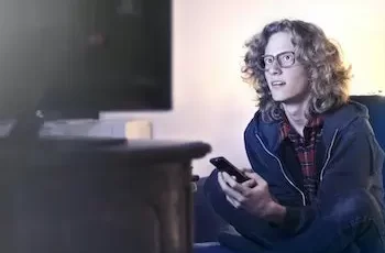 homem assiste TV no sofá com controle remoto na mão